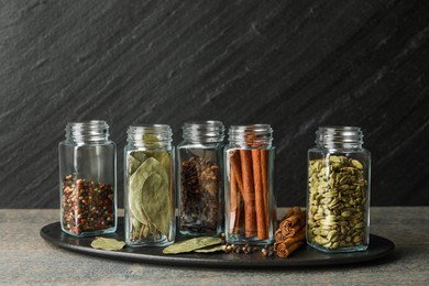 Photo of Different spices in glass jars on grey wooden table, closeup