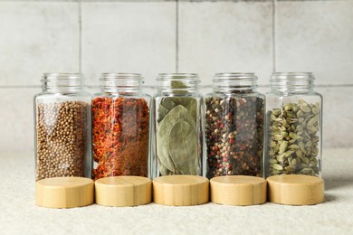 Photo of Different spices in glass jars and lids on light textured table, closeup