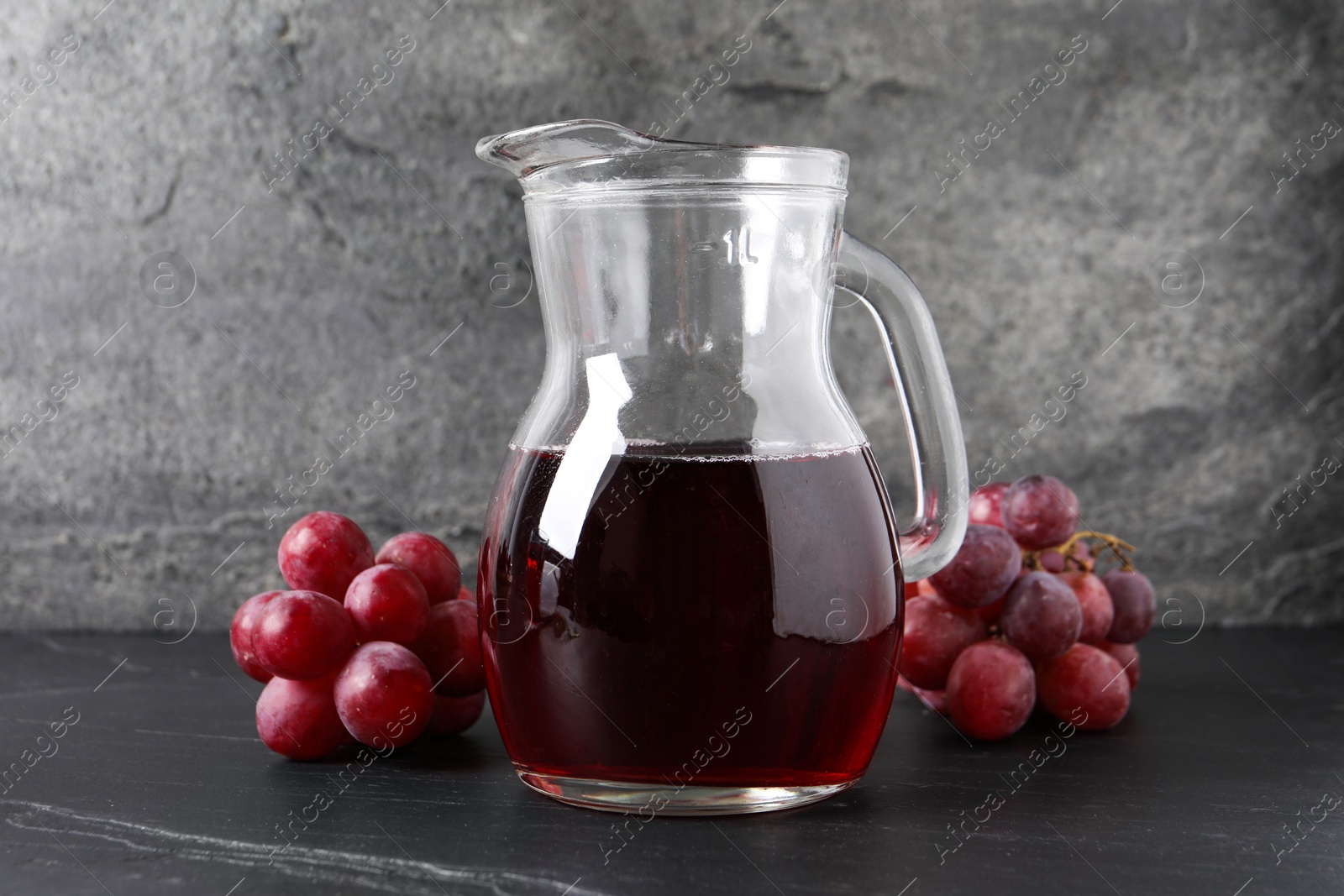 Photo of Tasty grape juice in jar and berries on dark textured table, closeup