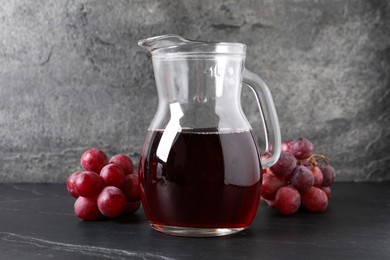 Tasty grape juice in jar and berries on dark textured table, closeup