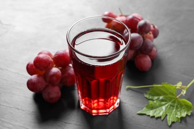 Tasty grape juice in glass, leaf and berries on dark textured table, closeup