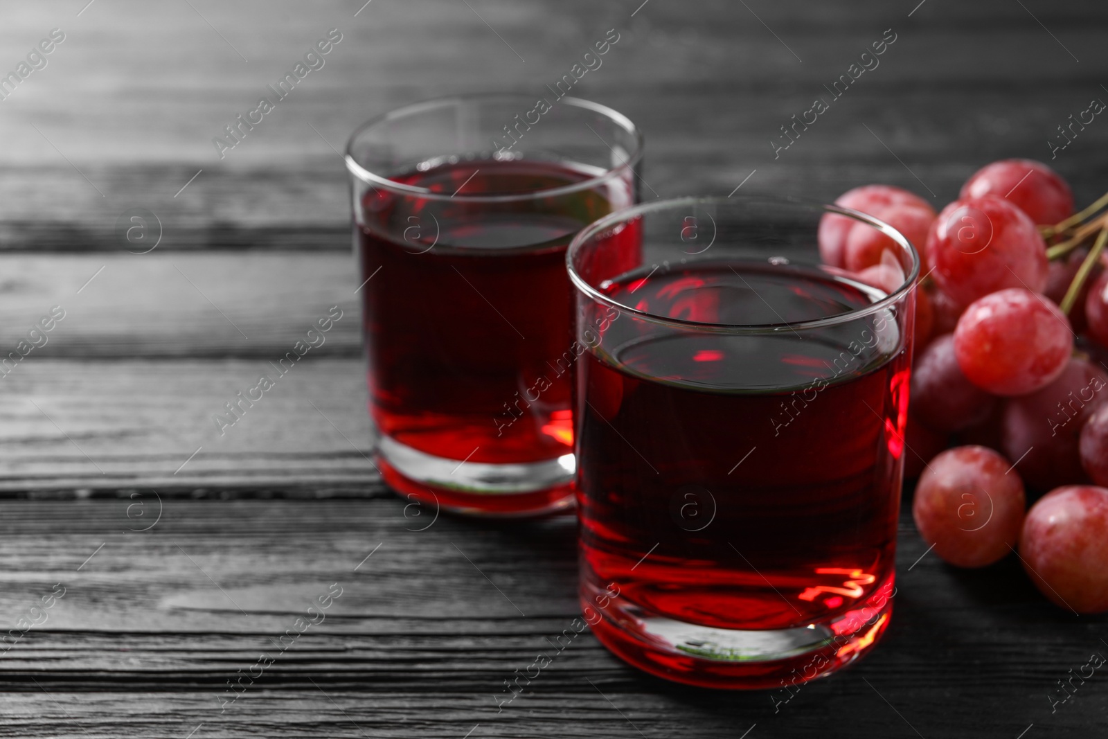 Photo of Tasty grape juice in glasses and berries on black wooden table, closeup