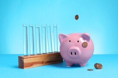 Photo of Water save concept. Piggy bank, coins and liquid in test tubes on light blue background