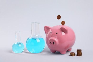 Photo of Water save concept. Piggy bank, coins and laboratory glassware with liquid on light grey background