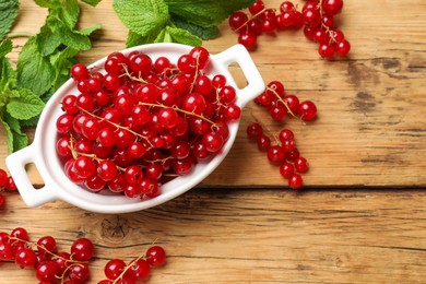 Photo of Fresh red currants in bowl and mint on wooden table, flat lay. Space for text