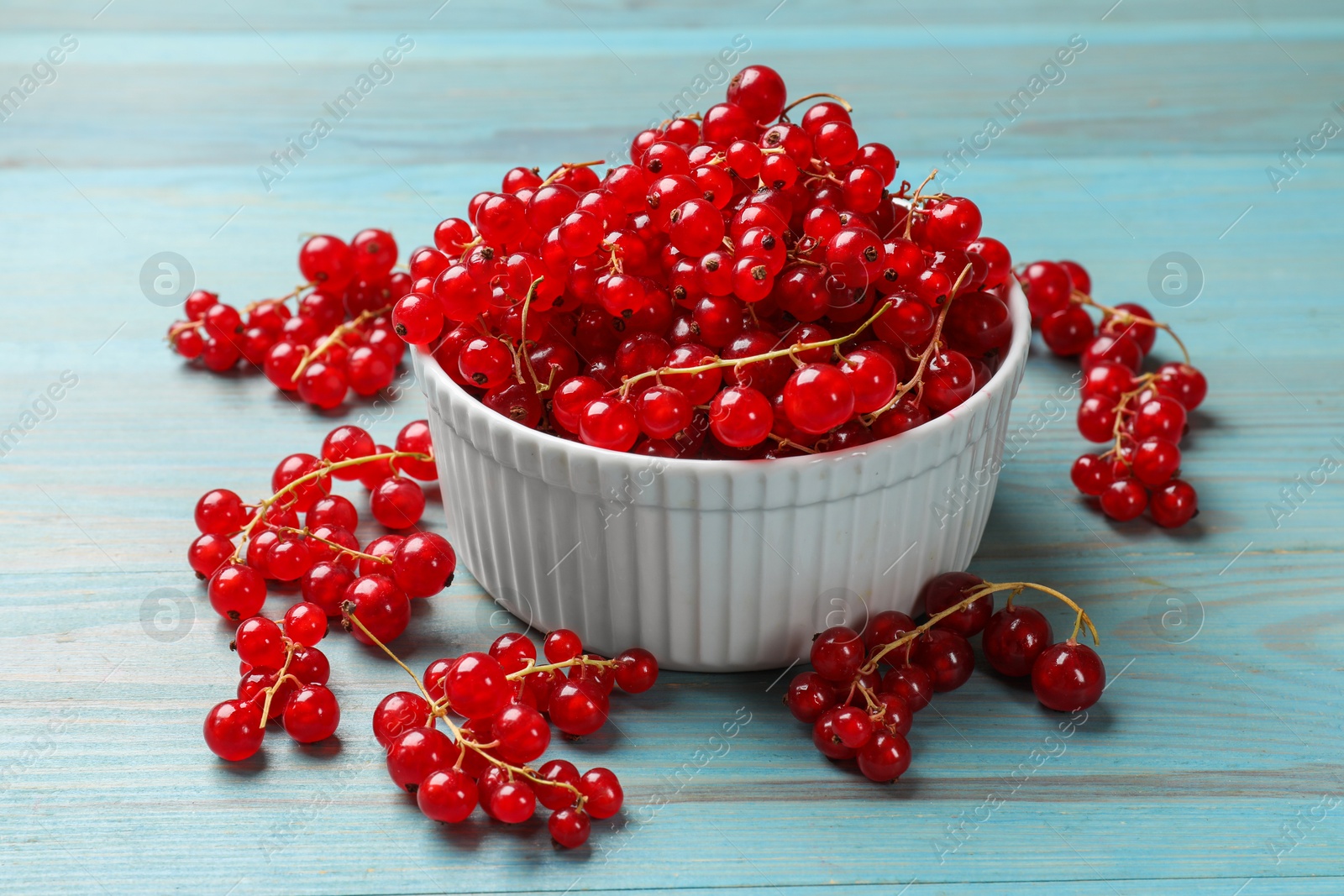 Photo of Fresh red currants in bowl on light blue wooden table