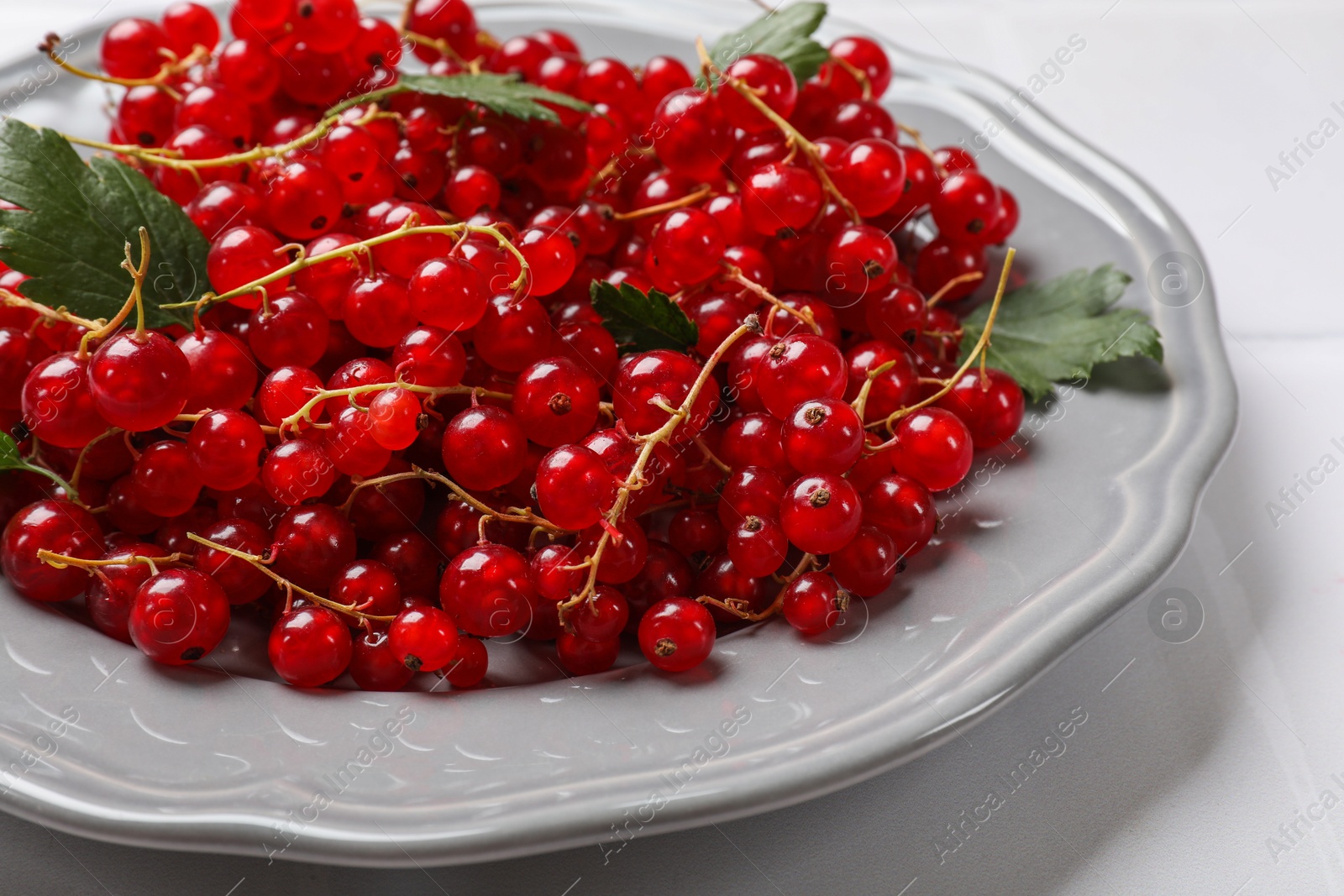 Photo of Fresh red currants and leaves on white table, closeup