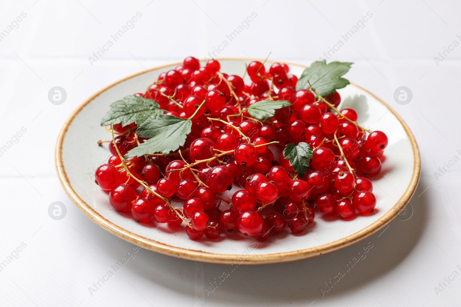 Photo of Fresh red currants and green leaves on white table, closeup