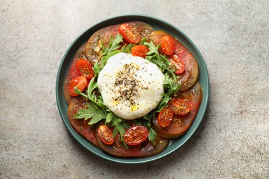 Photo of Delicious fresh burrata salad in bowl on gray textured table, top view