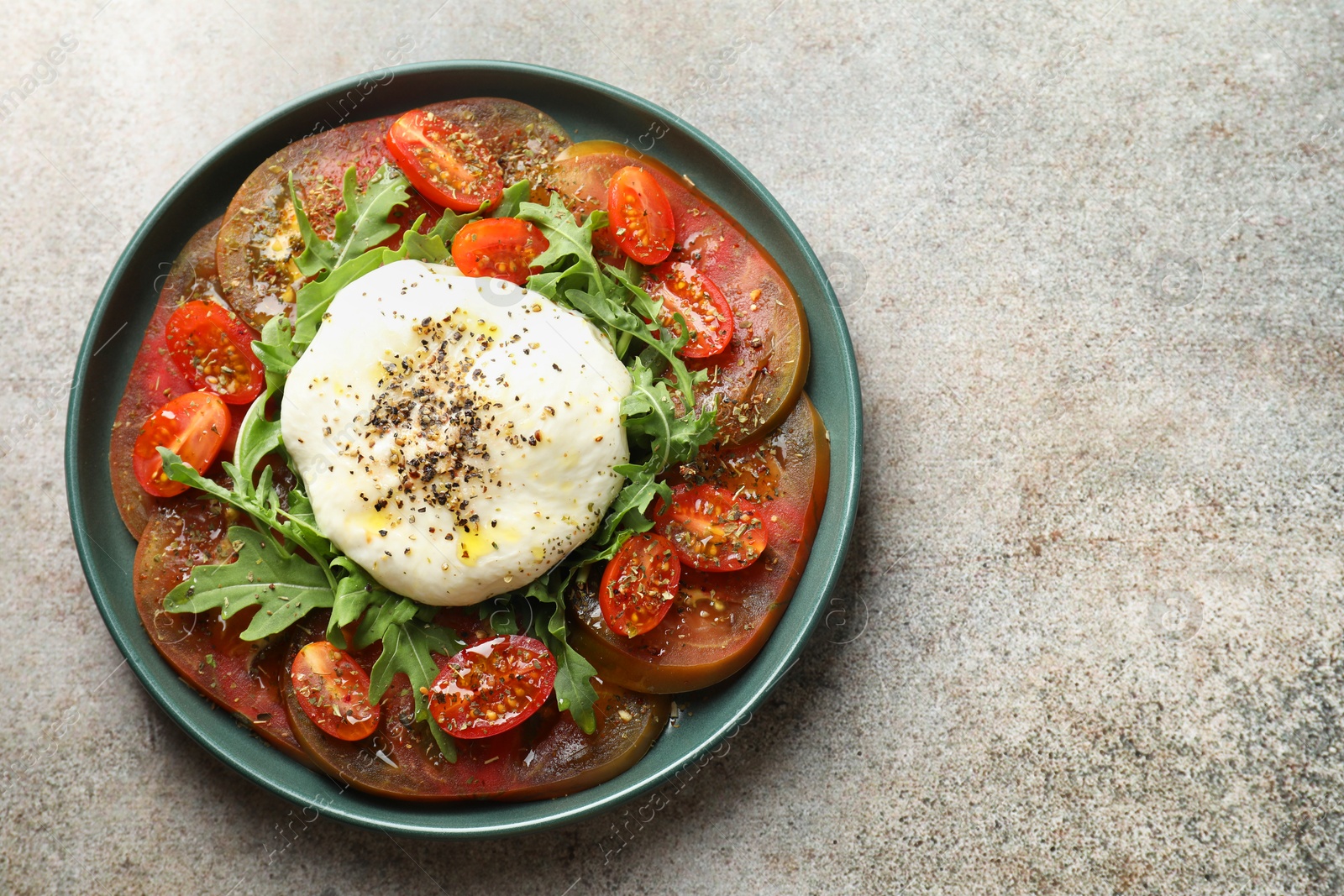 Photo of Delicious fresh burrata salad in bowl on gray textured table, top view. Space for text