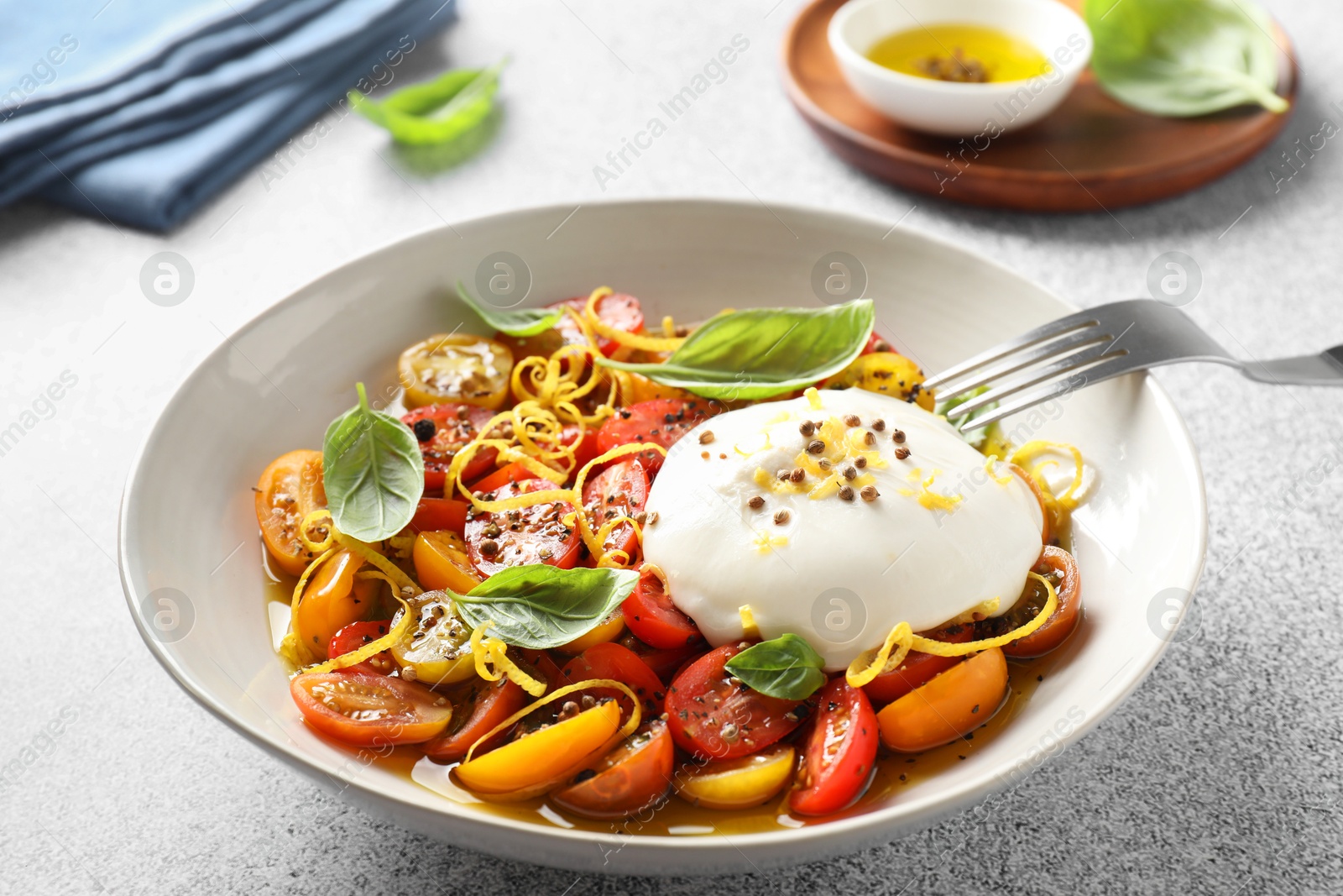 Photo of Delicious fresh burrata salad in bowl served on light gray textured table, closeup