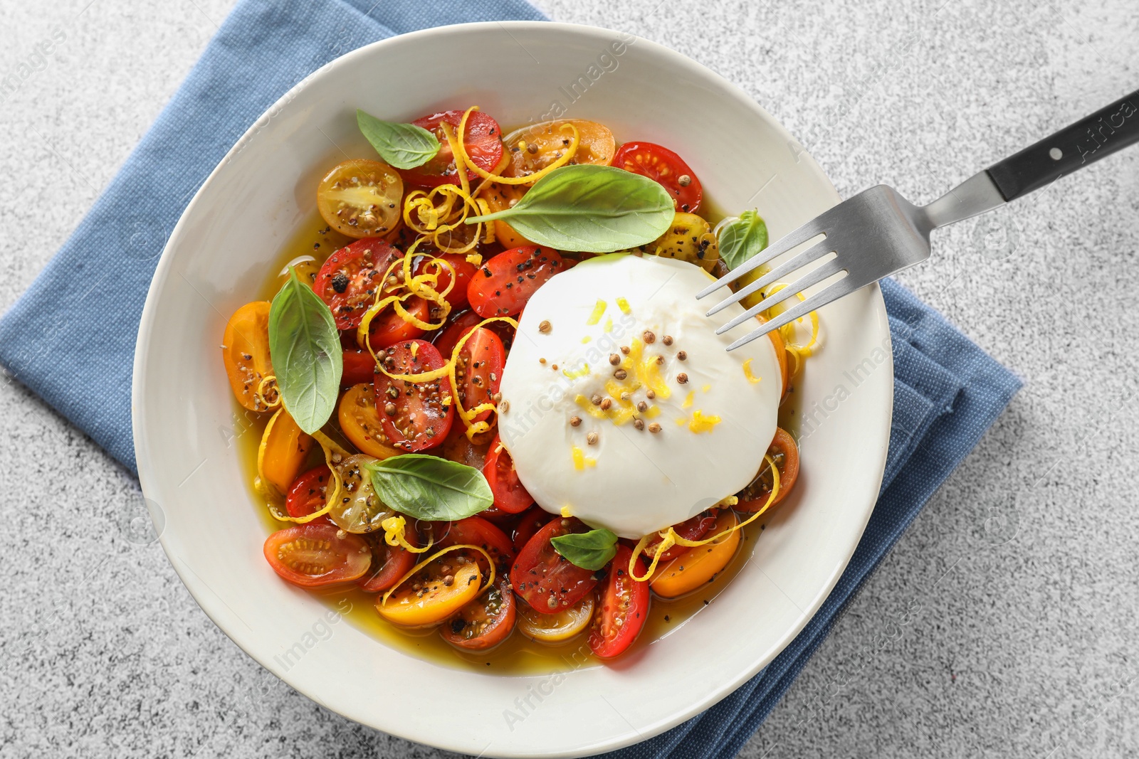 Photo of Delicious fresh burrata salad in bowl served on light gray textured table, top view