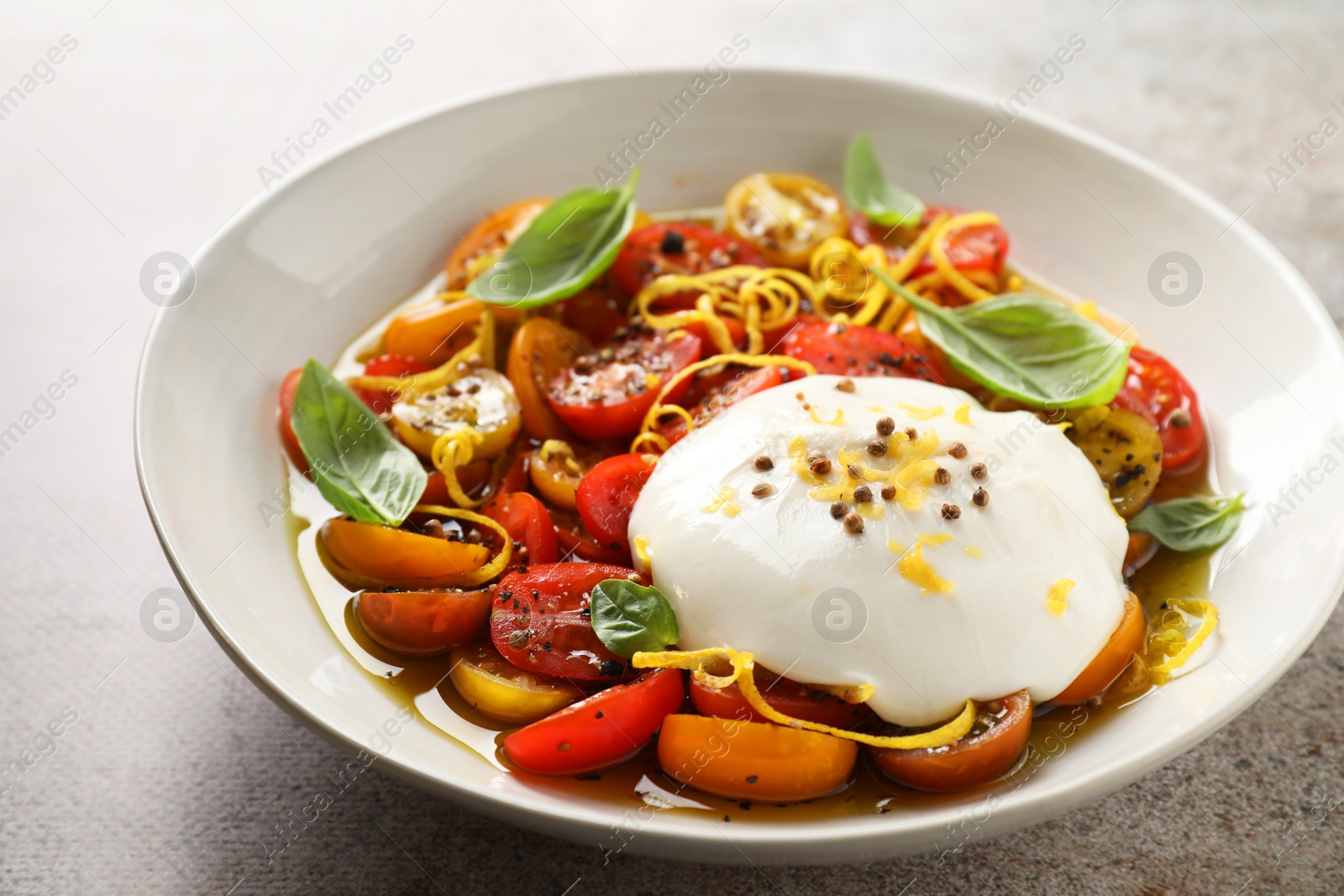 Photo of Delicious fresh burrata salad in bowl on gray textured table, closeup