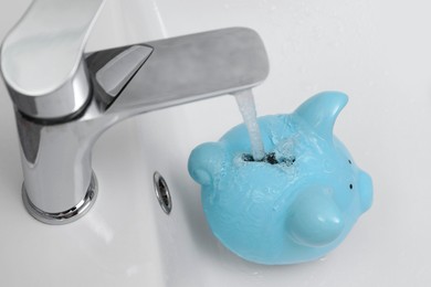 Photo of Water saving concept. Stream of water flowing from tap into piggy bank in bathroom, above view