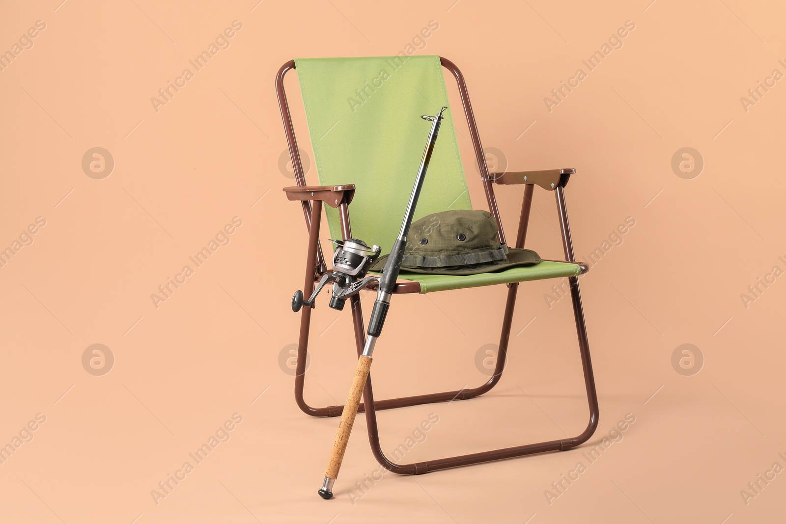 Photo of Folding chair, fishing rod and hat on beige background