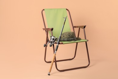 Photo of Folding chair, fishing rod and hat on beige background