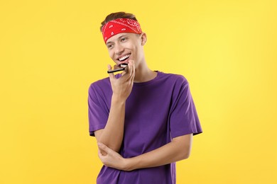 Photo of Young man recording voice message via smartphone on yellow background