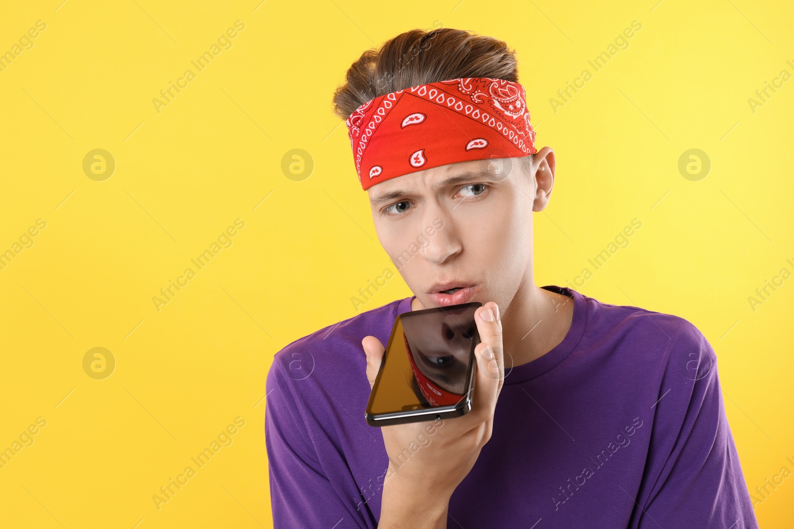 Photo of Young man recording voice message via smartphone on yellow background, space for text