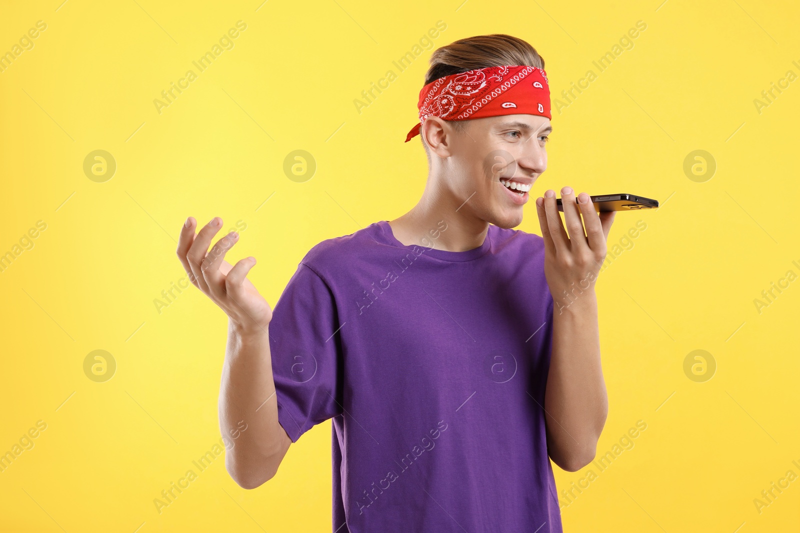 Photo of Young man recording voice message via smartphone on yellow background