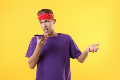 Photo of Young man recording voice message via smartphone on yellow background