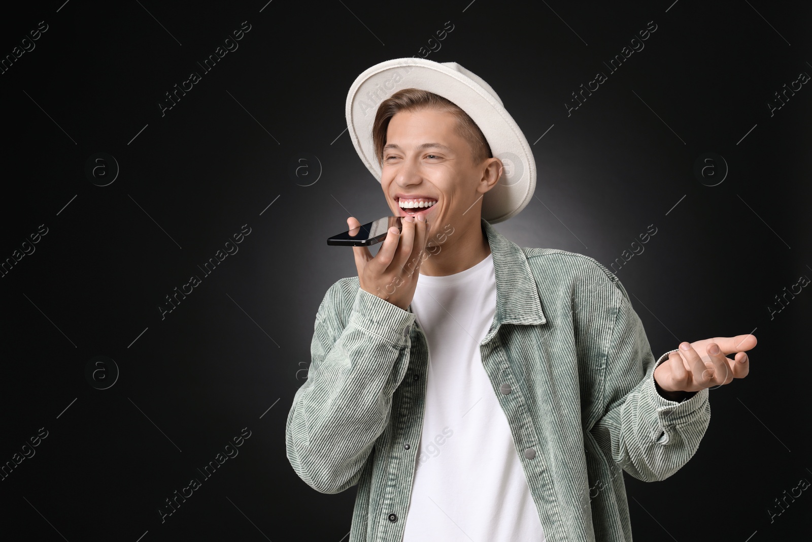 Photo of Young man recording voice message via smartphone on dark background, space for text