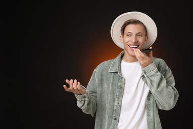 Young man recording voice message via smartphone on dark background, space for text