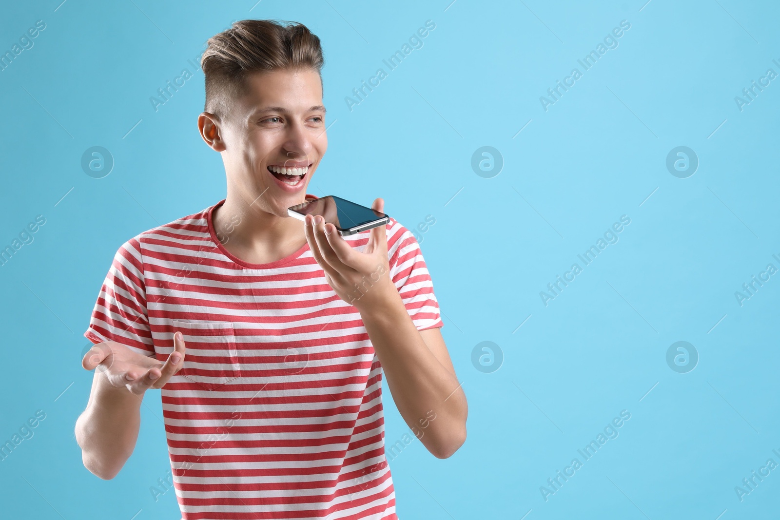 Photo of Young man recording voice message via smartphone on light blue background, space for text