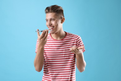 Young man recording voice message via smartphone on light blue background