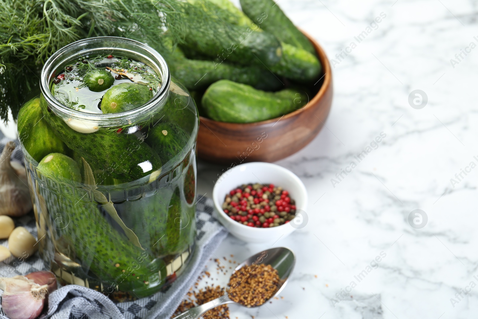 Photo of Making pickles. Fresh cucumbers and spices in jar on white marble table, space for text