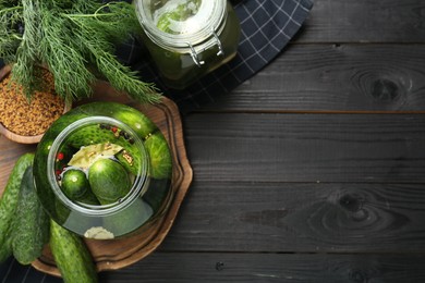 Photo of Making pickles. Fresh cucumbers and spices in jars on black wooden table, top view. Space for text