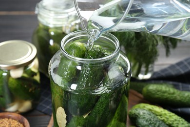 Photo of Making pickles. Pouring water into jar with cucumbers at table, closeup