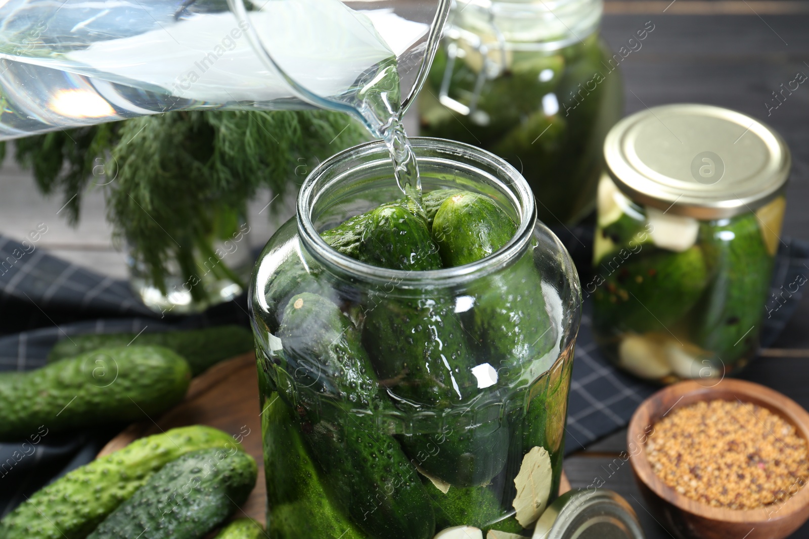 Photo of Making pickles. Pouring water into jar with cucumbers at table, closeup