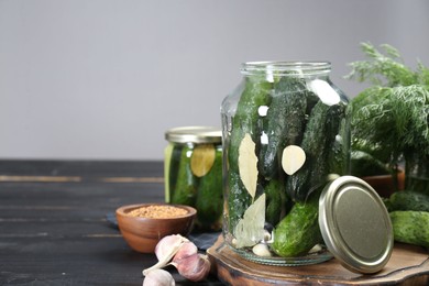 Photo of Making pickles. Fresh cucumbers and spices in jars on black wooden table. Space for text