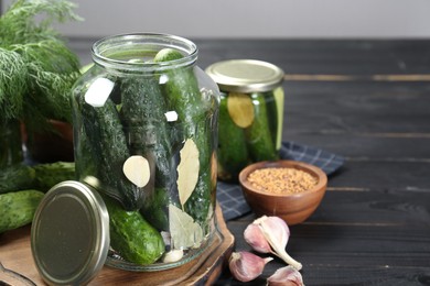 Photo of Making pickles. Fresh cucumbers and spices in jars on black wooden table