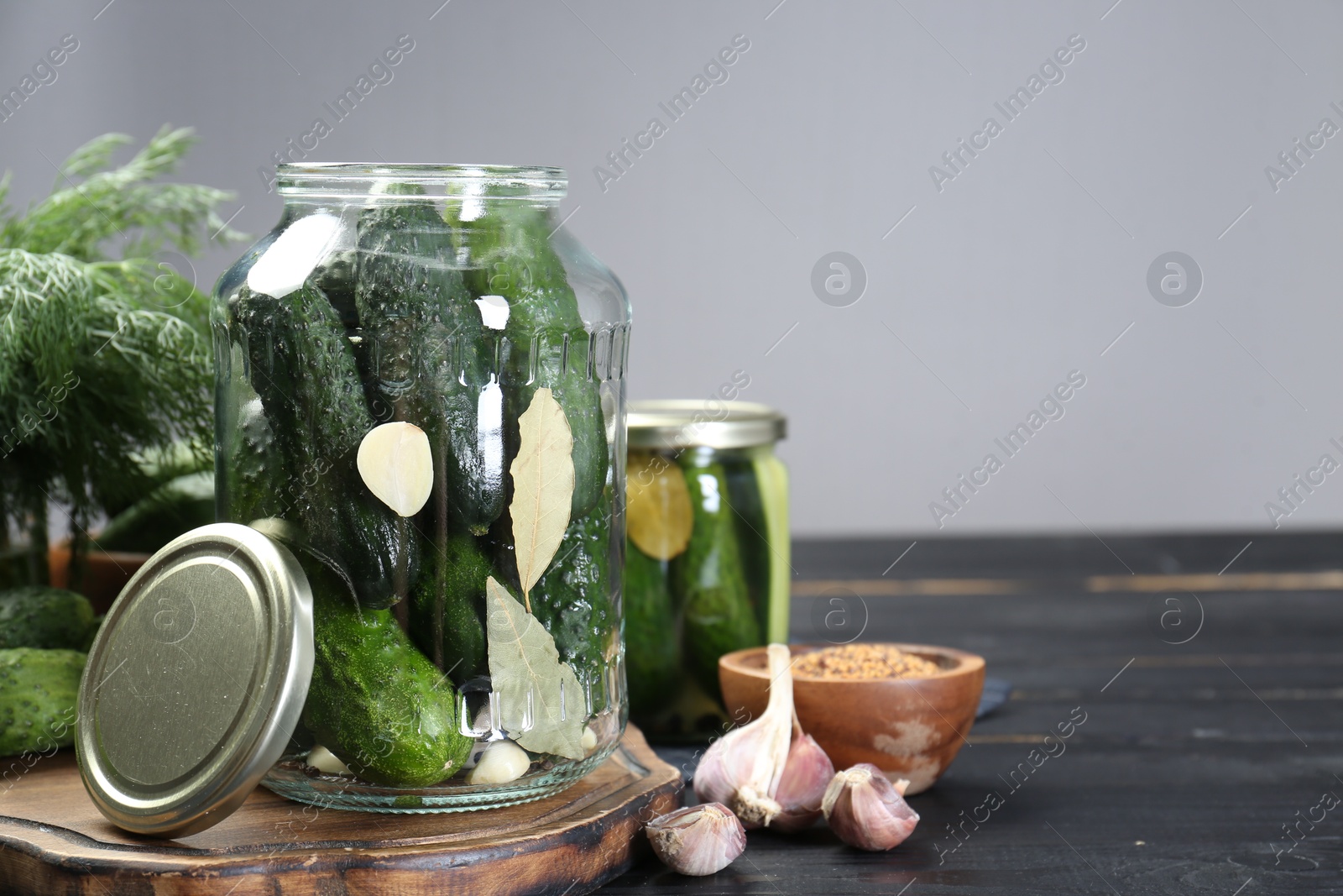 Photo of Making pickles. Fresh cucumbers and spices in jars on black wooden table