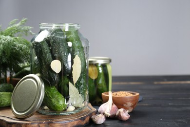 Photo of Making pickles. Fresh cucumbers and spices in jars on black wooden table