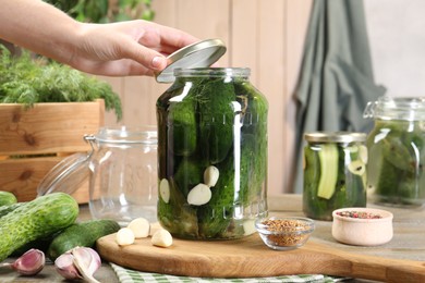 Photo of Woman pickling cucumbers at wooden table, closeup