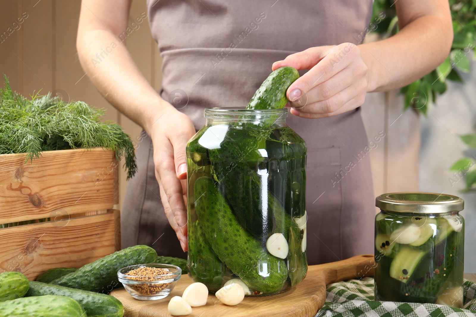 Photo of Making pickles. Woman putting cucumber into glass jar at table, closeup