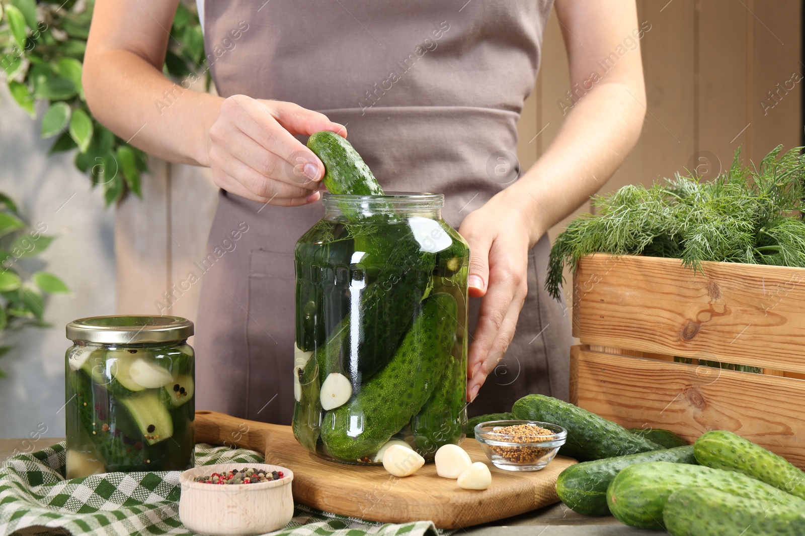 Photo of Making pickles. Woman putting cucumber into glass jar at table, closeup