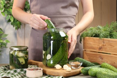 Photo of Making pickles. Woman putting cucumber into glass jar at table, closeup