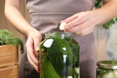 Photo of Making pickles. Woman putting garlic into glass jar at table, closeup