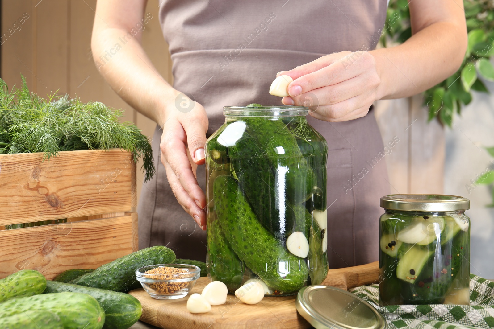 Photo of Making pickles. Woman putting garlic into glass jar at table, closeup