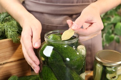 Photo of Making pickles. Woman putting bay leaf into glass jar at table, closeup