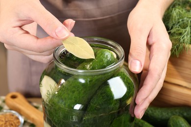 Photo of Making pickles. Woman putting bay leaf into glass jar at table, closeup