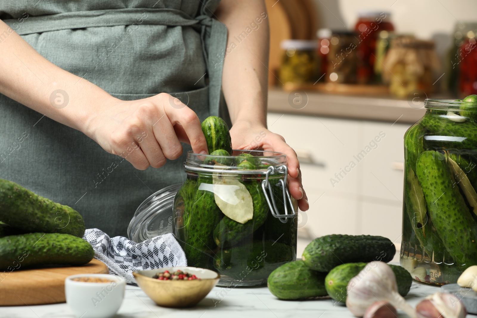 Photo of Making pickles. Woman putting cucumber into glass jar at white marble table, closeup