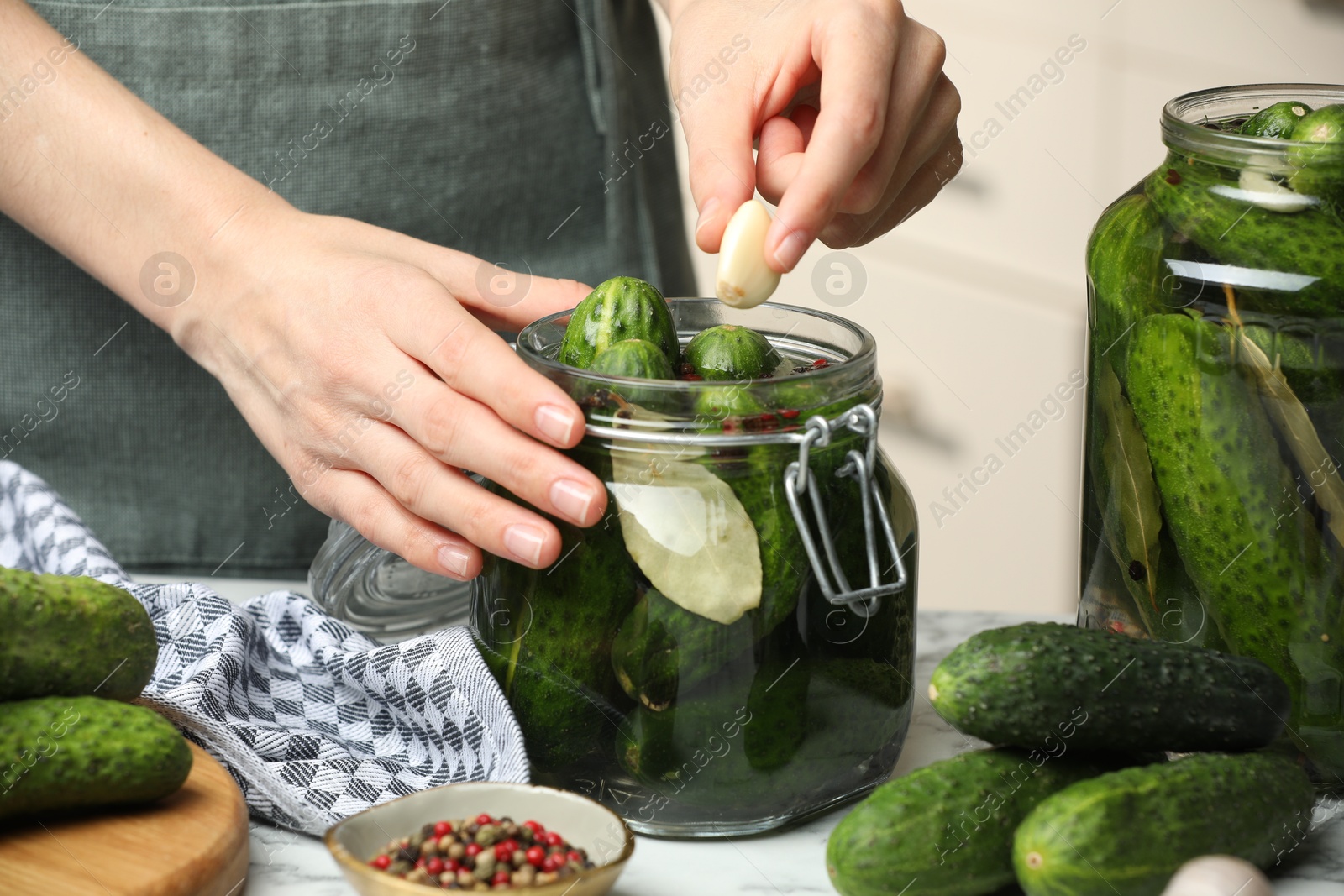 Photo of Making pickles. Woman putting garlic into glass jar at table, closeup