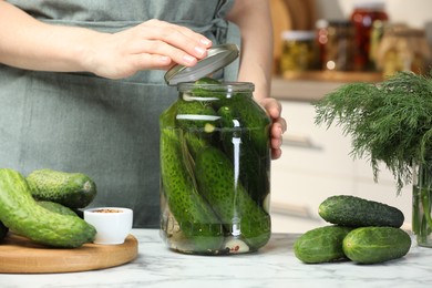 Photo of Woman pickling glass jar of cucumbers at white marble table, closeup