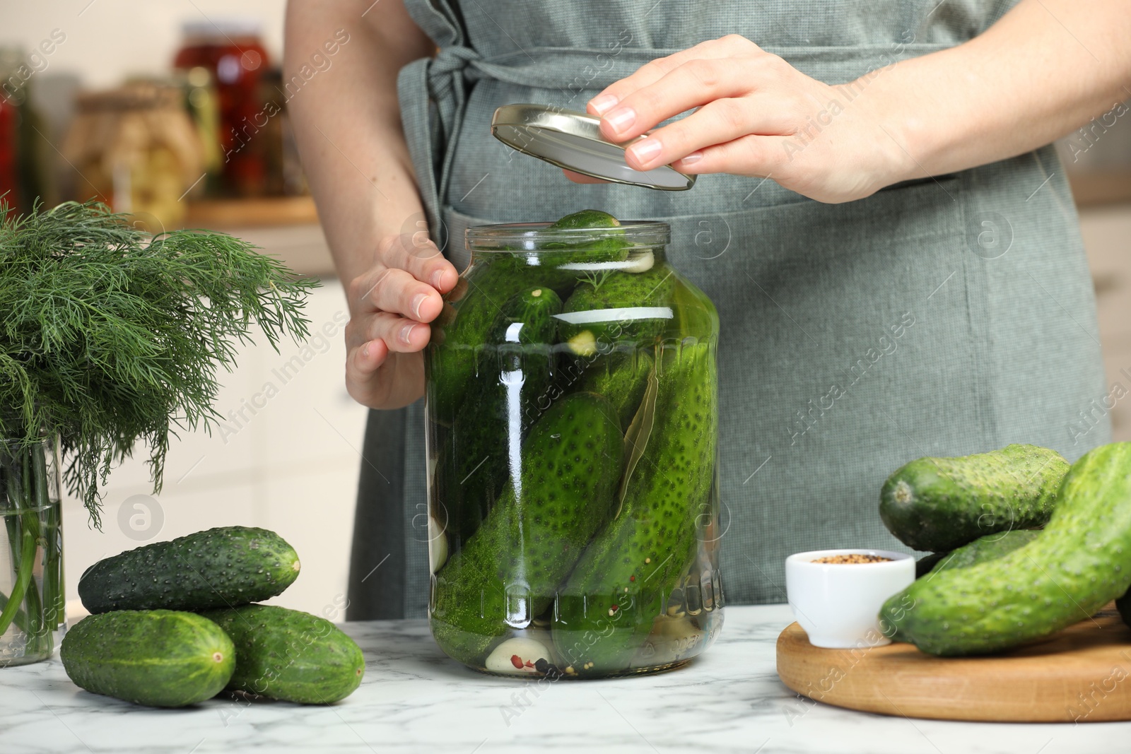 Photo of Woman pickling glass jar of cucumbers at white marble table, closeup