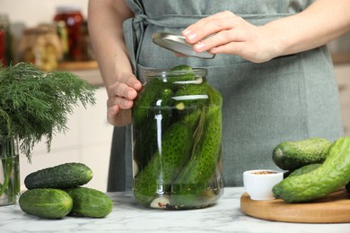 Photo of Woman pickling glass jar of cucumbers at white marble table, closeup