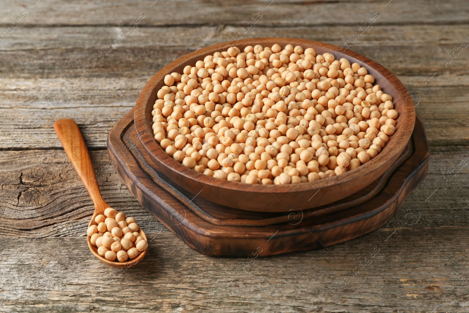 Photo of Dried peas in bowl and spoon on wooden table, closeup